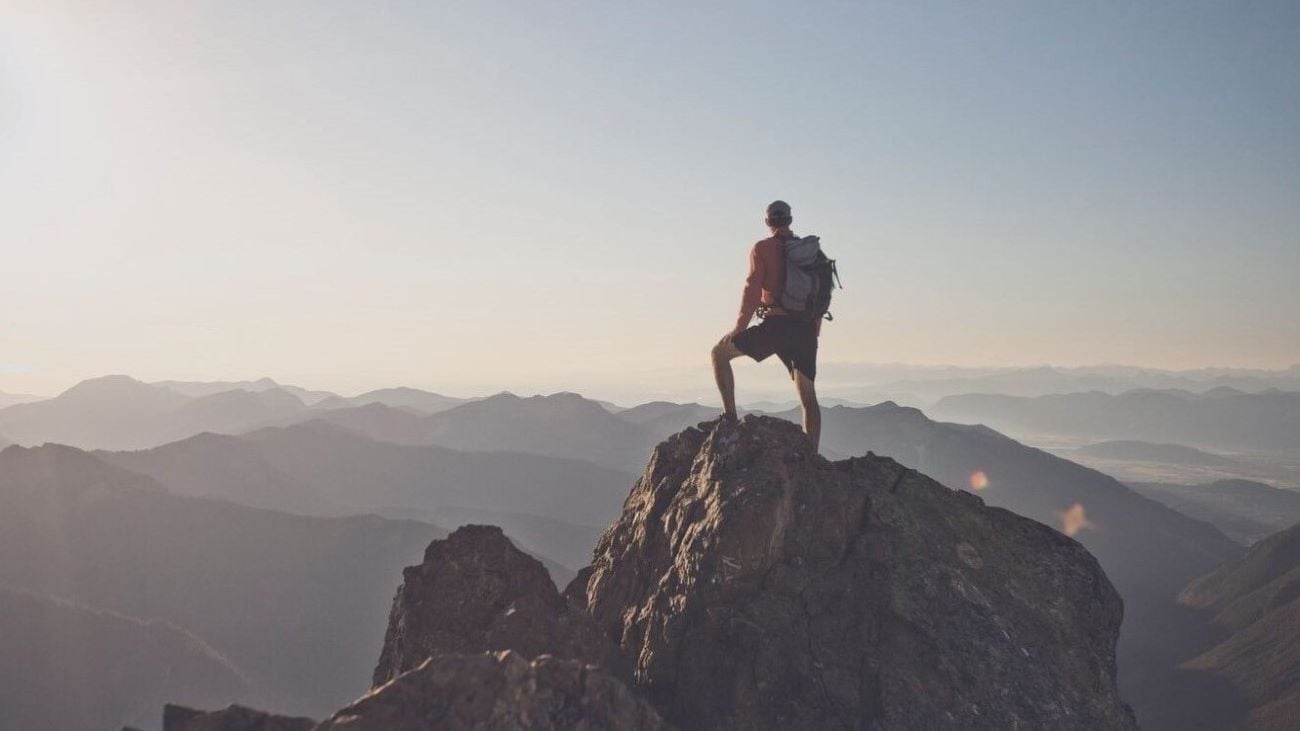 En mann som står på en fjelltopp og ser utover landskapet.