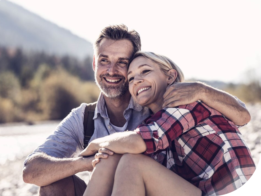 Mann og kvinne sitter ute i naturen og smiler mens de holder rundt hverandre 