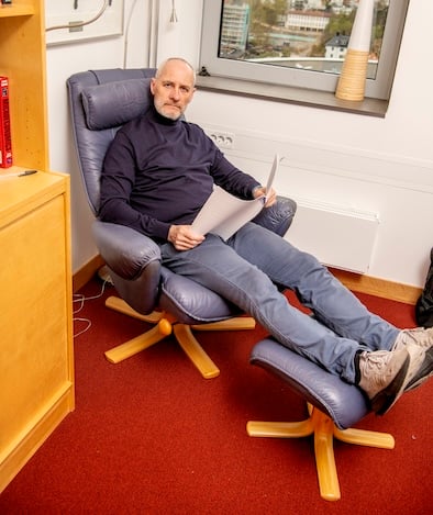 Mann sittende i lenestol på kontor. 