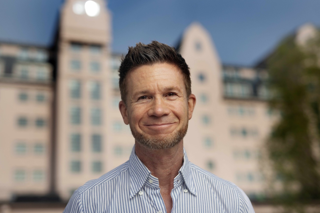 Mann som står rett i ryggen og smiler til kamera.