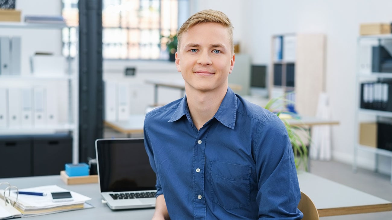 Portrettbilde av smilende ung mann sittende forran datamaskin