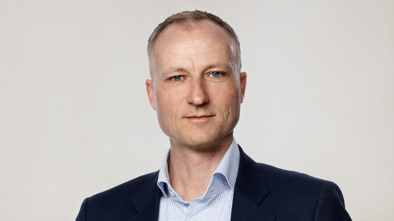 Portrettfoto av formelt kledd mann som smiler med øynene til kamera.