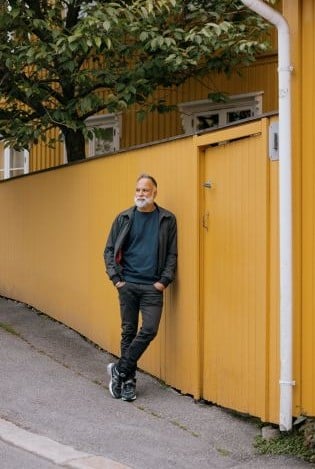 Mann som lener seg på gul trevegg i urbant strøk.