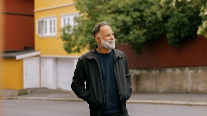 KJEMPER PÅ KAMPEN Smilende mann i utendørs urbant strøk med hendene i jakkelommen