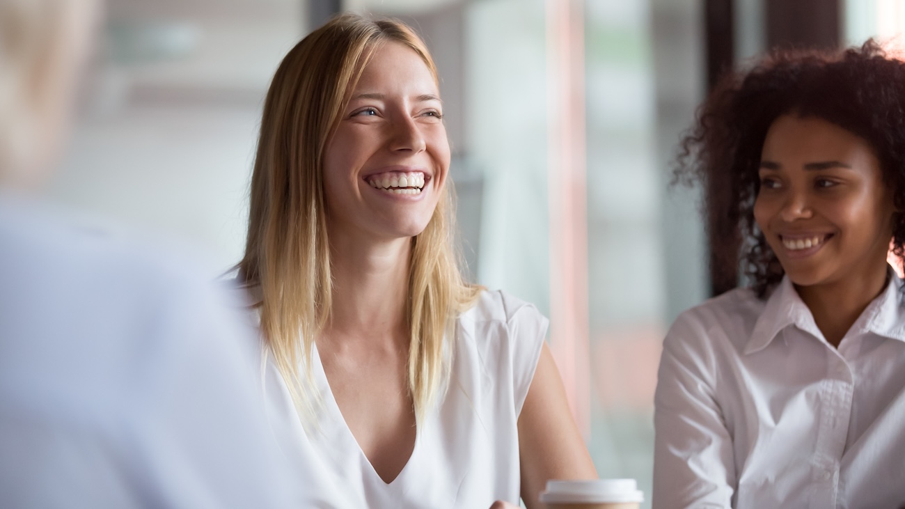 Smilende kvinne ved siden av en kollega i et møte.