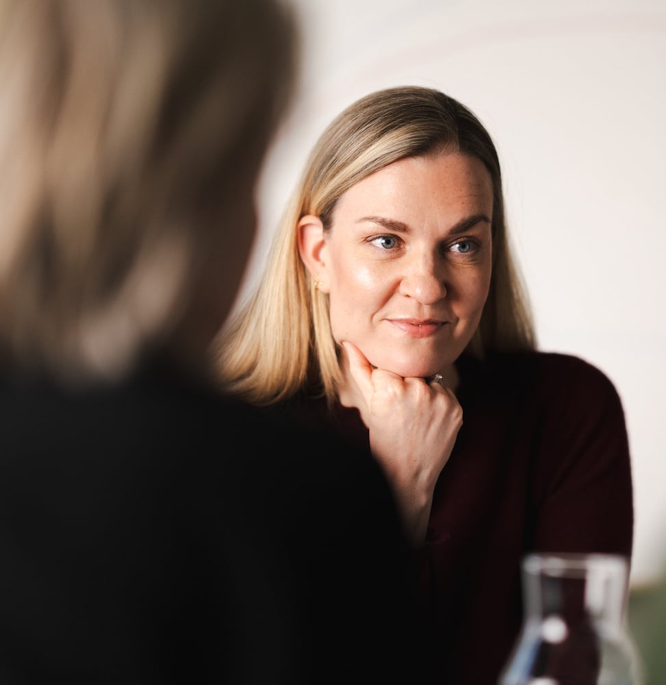 Kvinne som sitter og smiler mens hun lener seg på bordet foran henne.