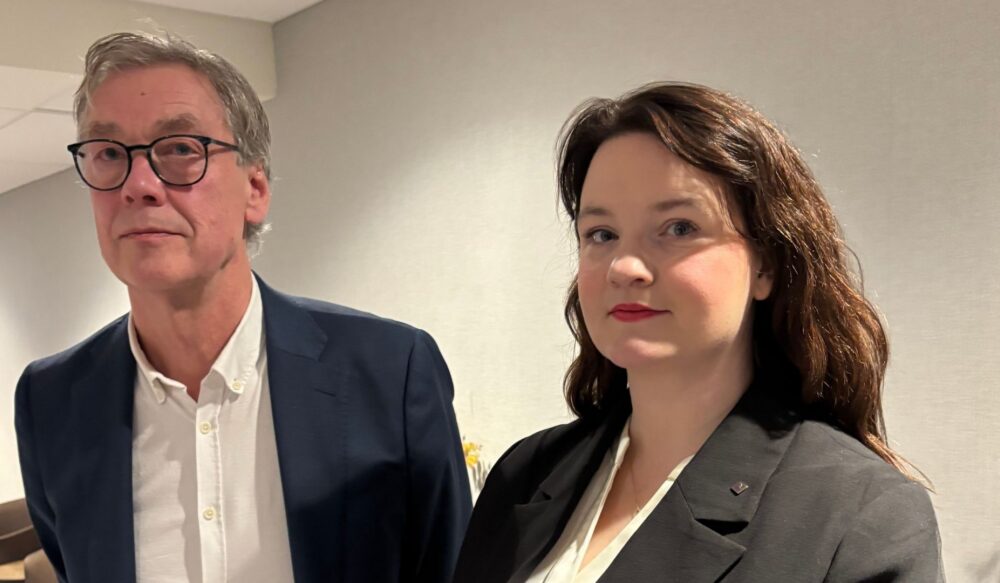 To personer i formell bekledning poserer foran en lys vegg, i forbindelse med ny hovedavtale mellom Econa og Spekter.