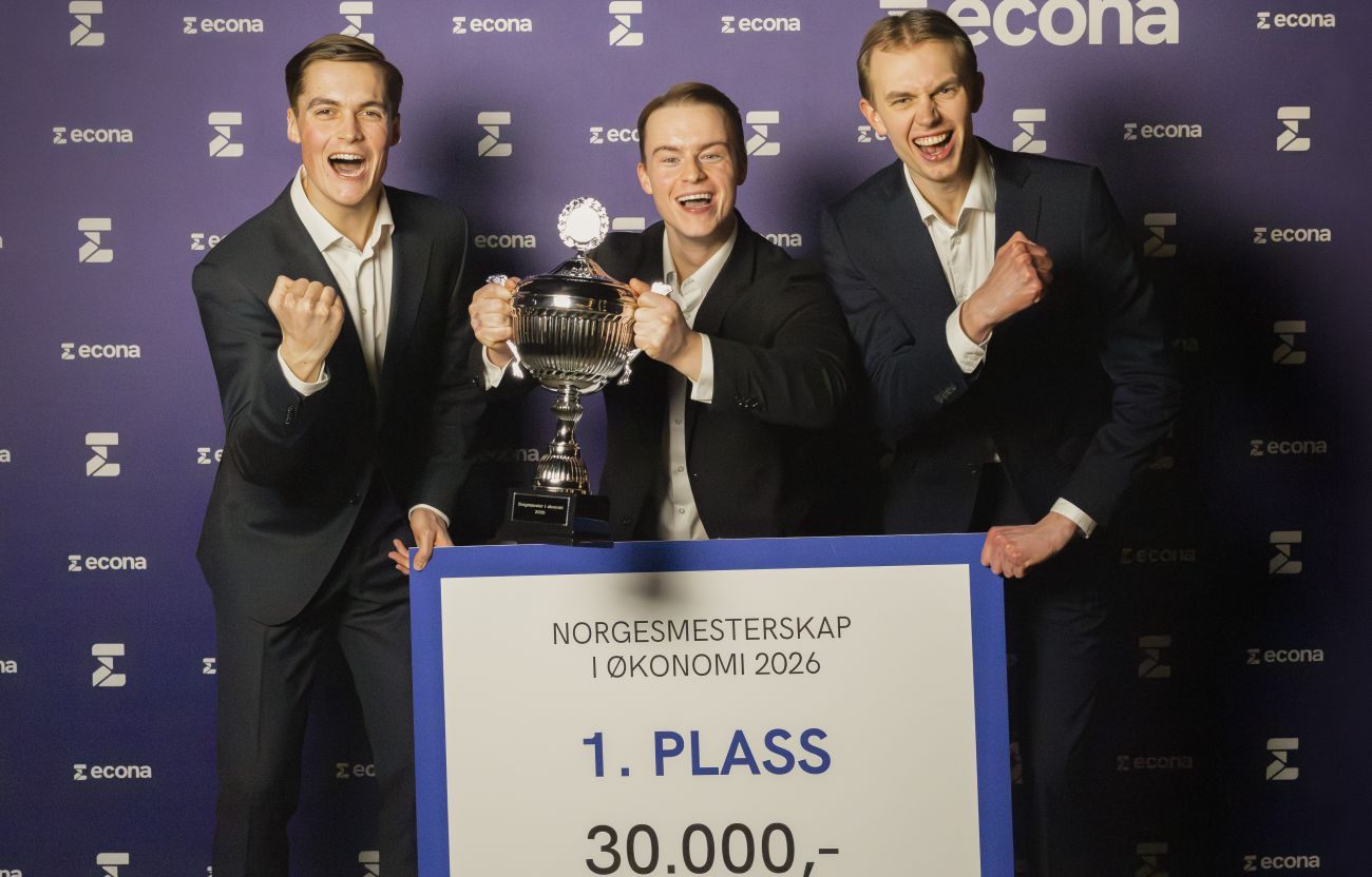 Tre unge menn, kledd i dress, som har vunnet NM i økonomi 2026 og jubler mens de holder pokalen.