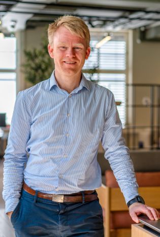 Mann som lener seg mot en stol i et lyst kontorlandskap mens han smiler til kamera.