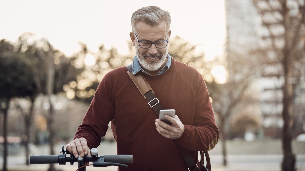 Mann som fører sykkelen sin med den ene hånden og ser ned på mobilen i andre hånden