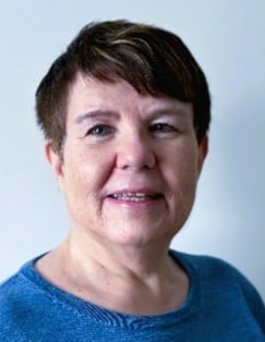 Portrettfoto av kvinne med kort hår som smiler forsiktig til kamera.