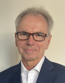 Portrettfoto av formelt kledd mann som smiler til kamera med lukket munn.