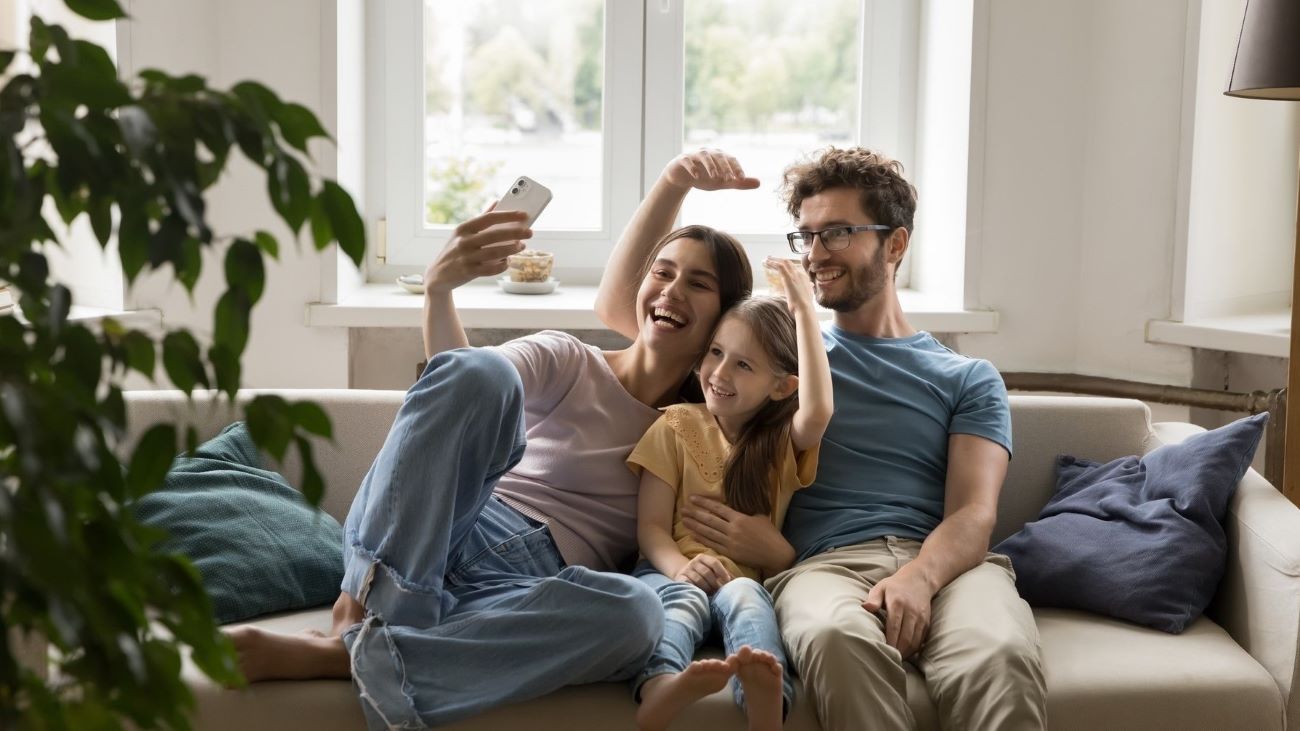 Glad familie på tre som sitter i sofaen og tar morsomme bilder av seg. 