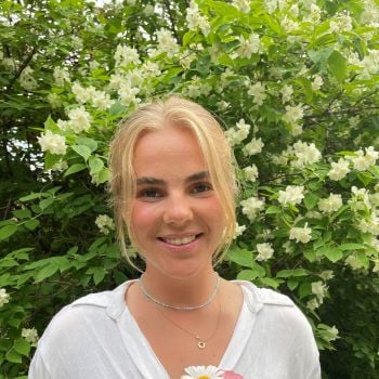 Ung kvinne som smiler til kamera og holder en liten blomsterbukett.