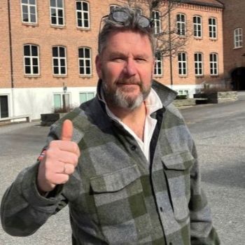 Mann som står ute i en skolegård og holder en tommel opp til kamera.
