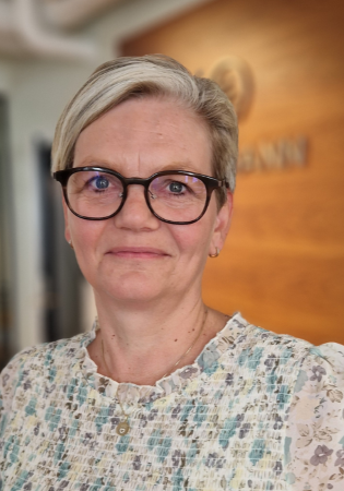 Nærfoto av kvinne i blomstrete bluse som smiler forsiktig til kamera.