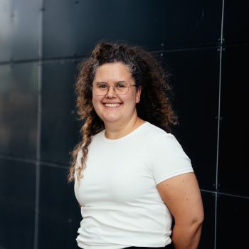 Kvinne som står med hendene bak ryggen og smiler bredt til kamera.