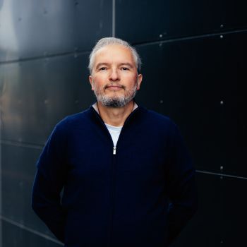 Portrettfoto av mann som står og smiler forsiktig til kamera mens han holder hendene bak ryggen.