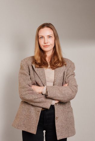 Ung kvinne som står med armene i kryss og smiler lurt til kamera.