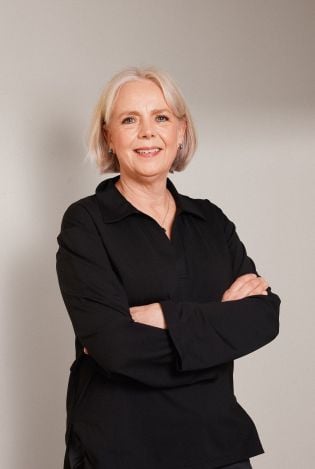 Portrettfoto av kvinne kledd i sort som står skrått vekk fra kamera med armene i kryss.