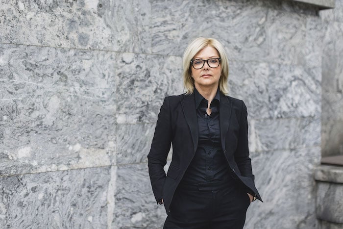Portrettbilde av Nina Riibe kledd i svart mot grå steinvegg