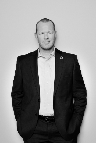 Svart-hvitt portrettfoto av smilende mann i dress.