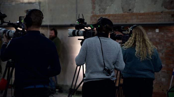 To kameramenn og en kamerakvinne som står og filmer et realityshow i et studio.