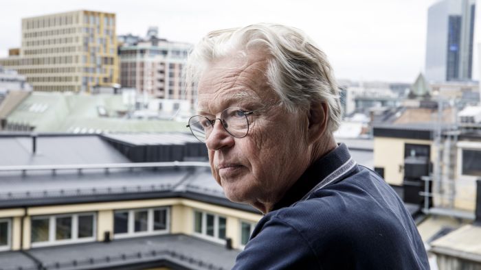 Eldre mann med briller som står på en takterasse.