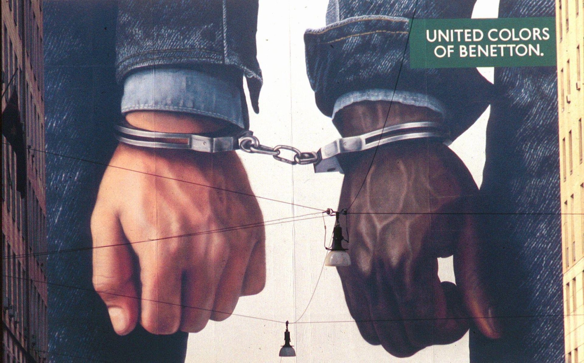 United Colors of Benetton sin gamle reklameplakat av en hvit og en mørkhudet hånd festet i håndjern. Illustrerer standpunkt mot rasisme.