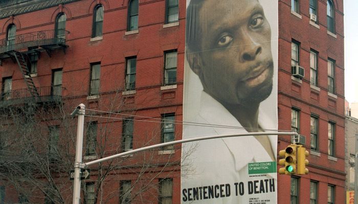 En stor reklameplakat på et rødt bygg av en mann med teksten "Sentenced to Death" fra United Colors of Benetton.
