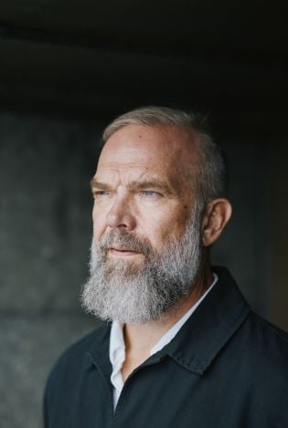 Nærbilde av mann som er hvit i håret og skjegget, og som ser utover med et alvorlig ansiktsuttrykk.