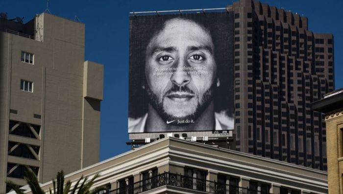 Nike reklameskilt i sort-hvitt med en mann og et sitat, på toppen av en bygning.