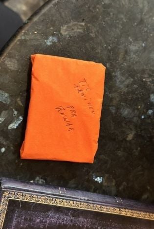 En liten gave pakket i oransje silkepapir som ligger på et marmorbord.