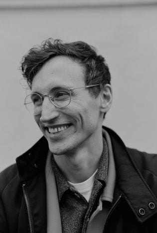 Nærbilde i svart-hvitt av mann som ser skrått vekk fra kamera og smiler bredt.