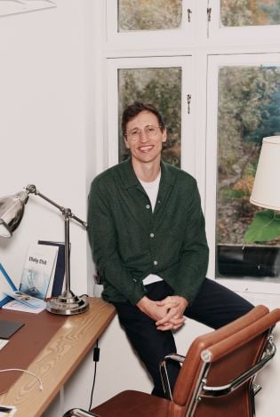 Mann som sitter i vinduskarmen på et hjemmekoselig kontor og smiler bredt til kamera.