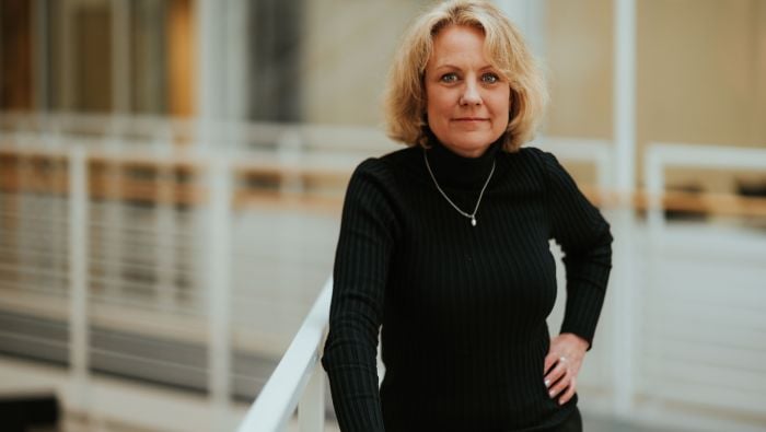 Kvinne som står og lener seg mot et gelender i et lyst kontorbygg. 