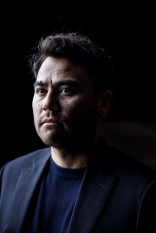 Portrettfoto av mann som står i et mørkt rom med et alvorlig uttrykk i ansiktet.