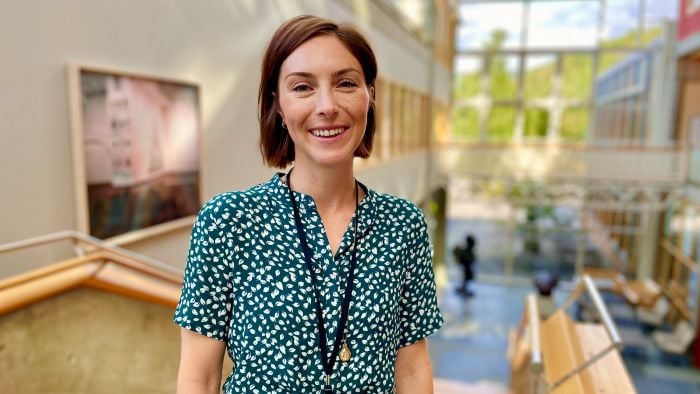 Kvinne som står i en trapp i et lyst kontorbygg og smiler bredt til kamera.