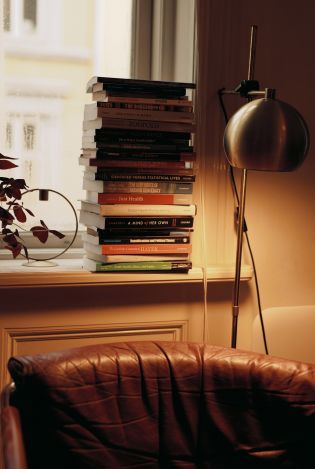 En sofakrok med dempet, lun belysning, og en stabel med bøker i vinduskarmen bak sofaen.