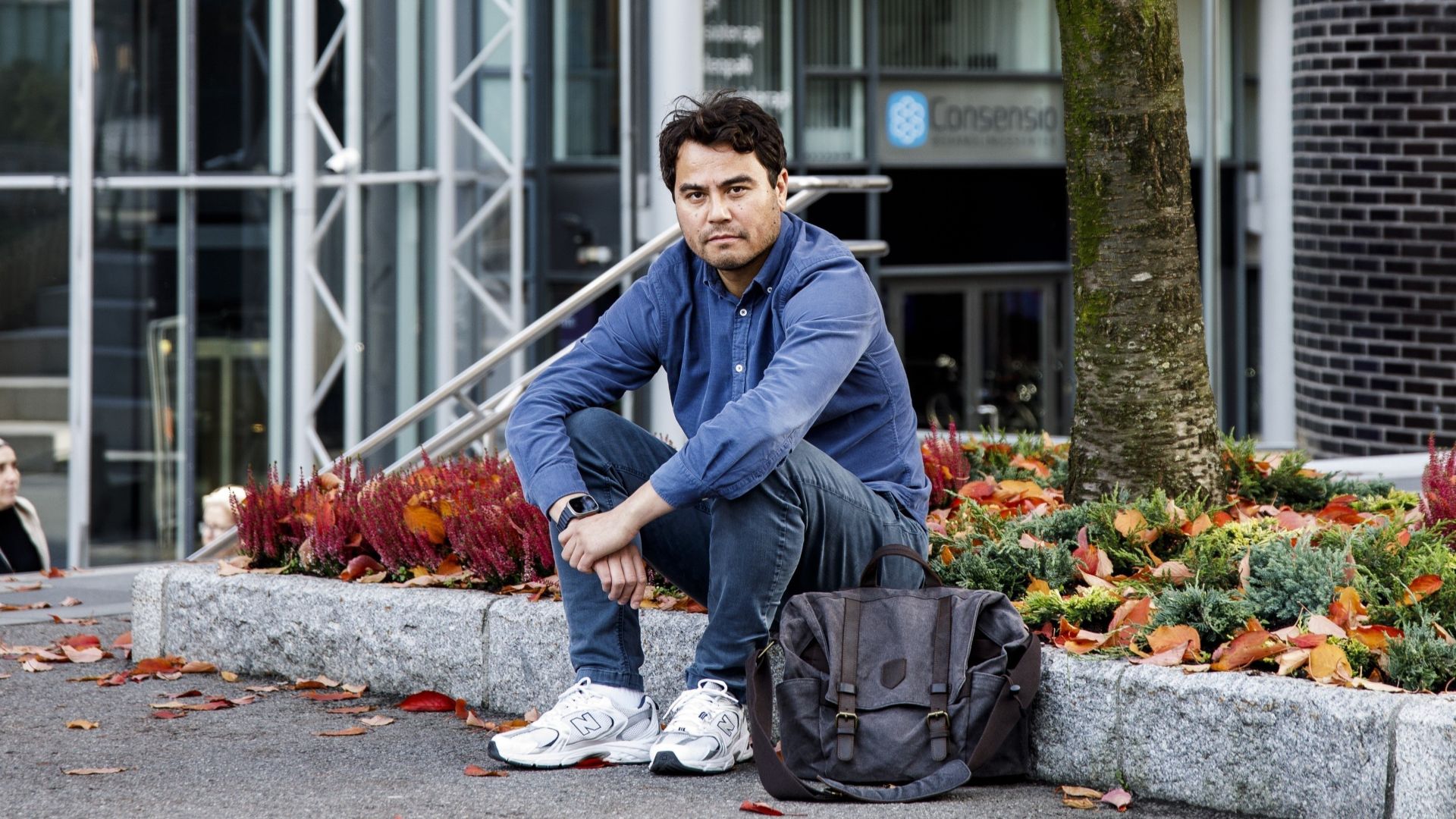 Mann som sitter på en steinhelle utenfor et bygg og ser alvorlig mot kamera.