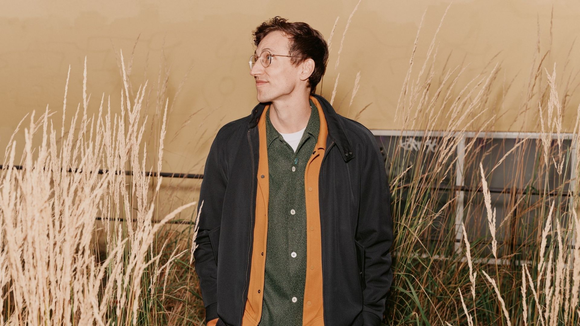 Mann som står med hendene i lommene foran et bygg og smiler med lukket munn.