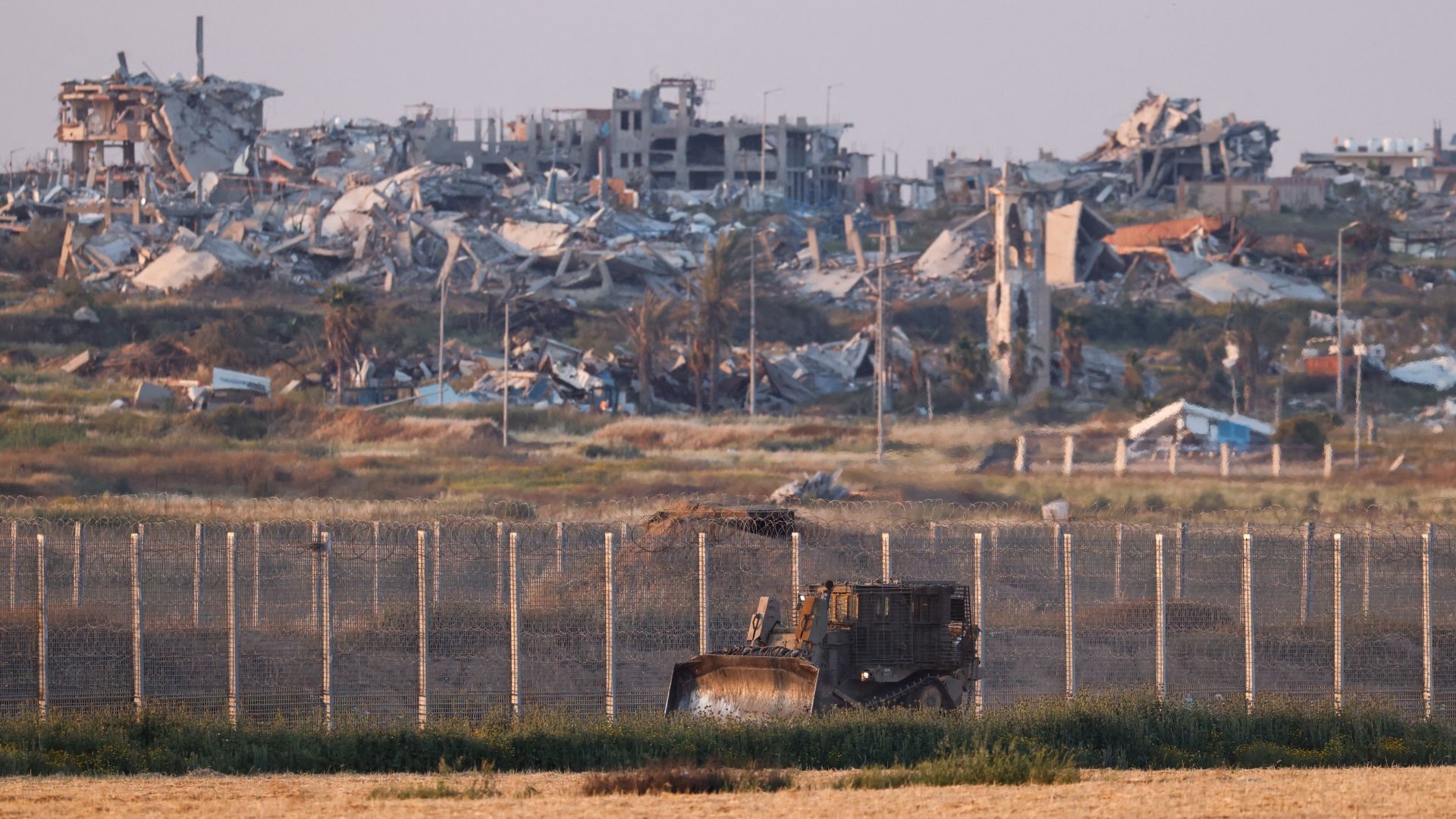 Gravmaskin foran et bombet boligområde i Gaza der kun ruinene av boligblokkene står igjen.