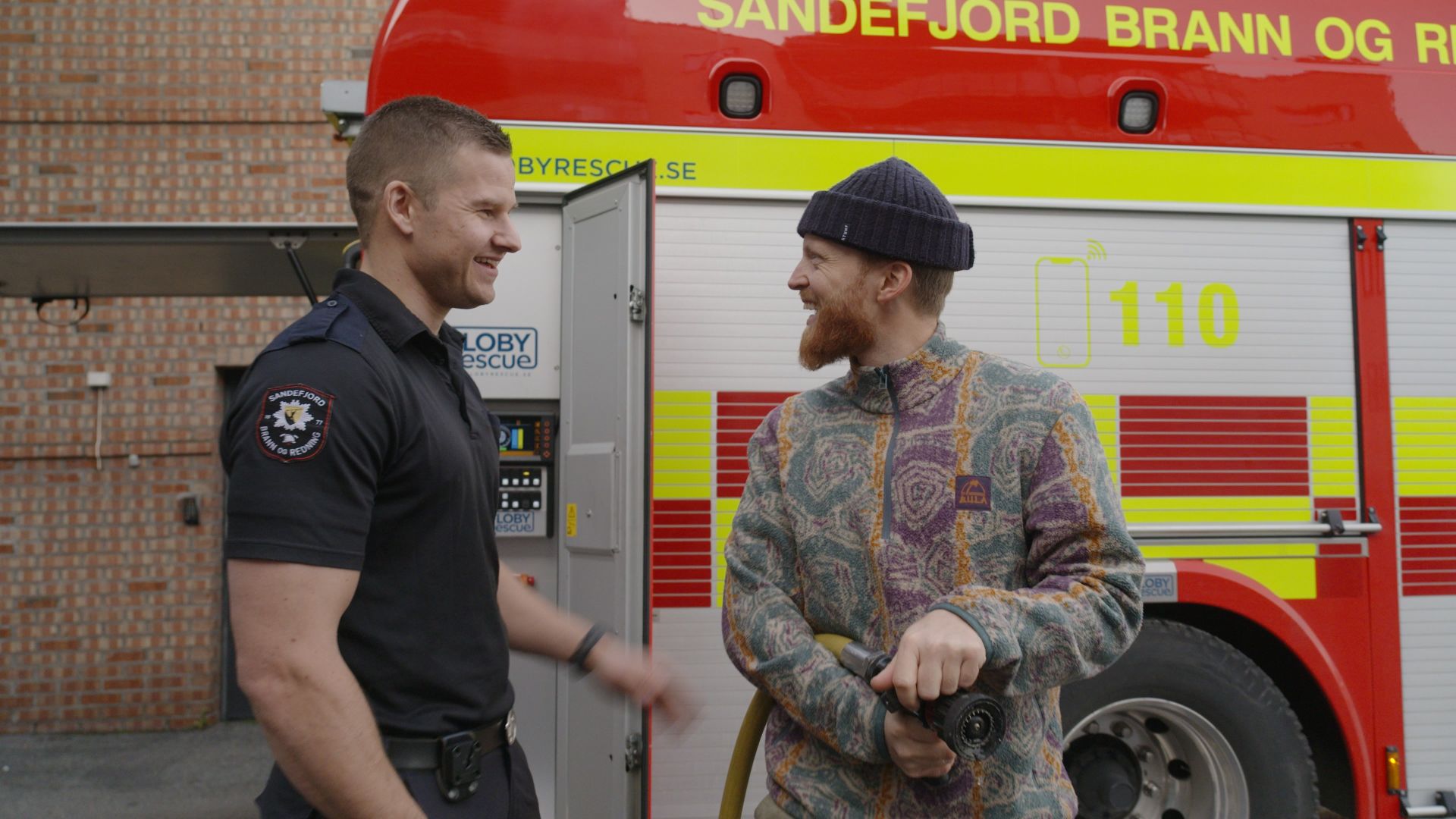 To menn som har en hyggelig samtale foran en brannbil.