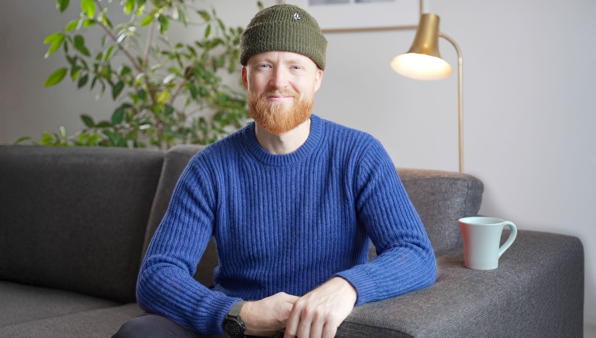 Ung mann som sitter i en sofa med kaffekoppen sin.