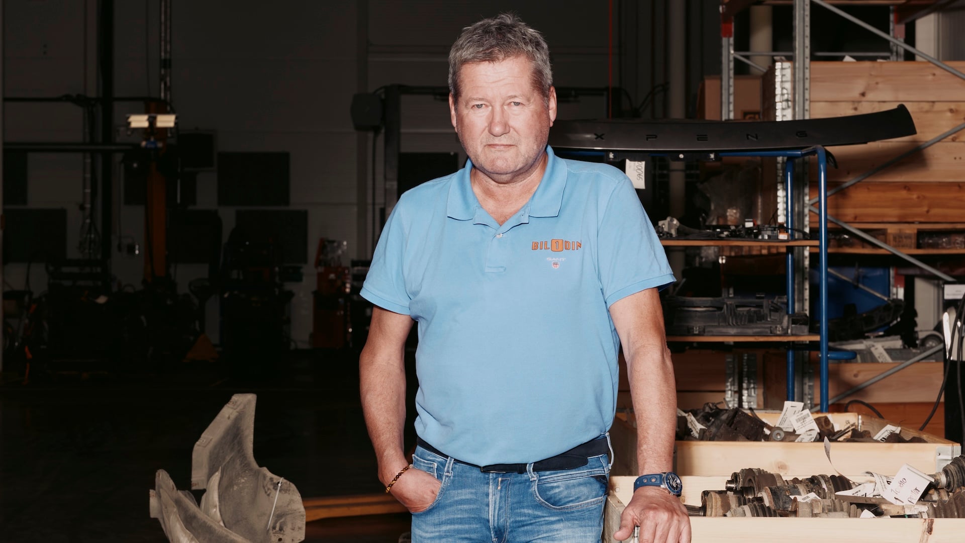 Bjarne Brøndbo som står inne på lageret i sin familiebedrift, omringet av bildeler.